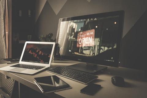 A desk with a desktop computer, keyboard, mouse, laptop computer, tablet computer, and smartphone