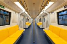 A view down an empty urban light rail carriage with yellow seats.