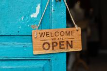 A blue door, from which hangs a wooden sign reading "welcome, we are open"